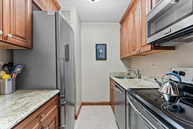 kitchen featuring appliances with stainless steel finishes, sink, light stone countertops, and a textured ceiling