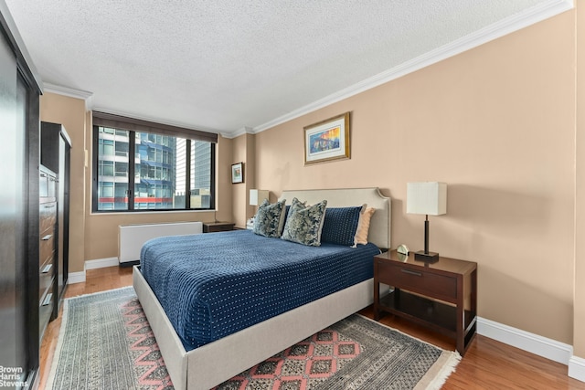 bedroom with a textured ceiling, radiator heating unit, light wood-style floors, and ornamental molding