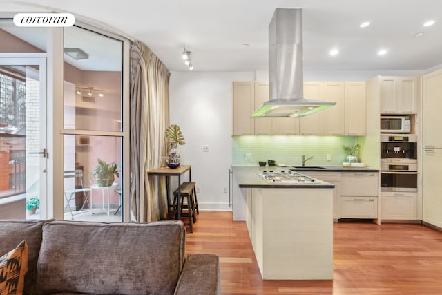 kitchen featuring island range hood, dark countertops, backsplash, a sink, and light wood-style floors