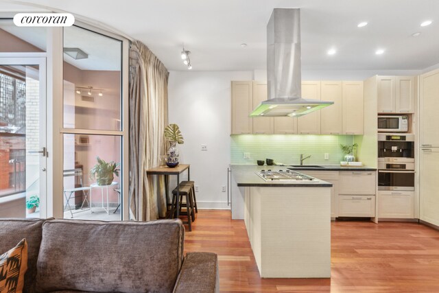 345 E 50th St Unit 5A, New York City, NY 10022 - kitchen with island exhaust hood, dark countertops, tasteful backsplash, light wood-type flooring, and white microwave