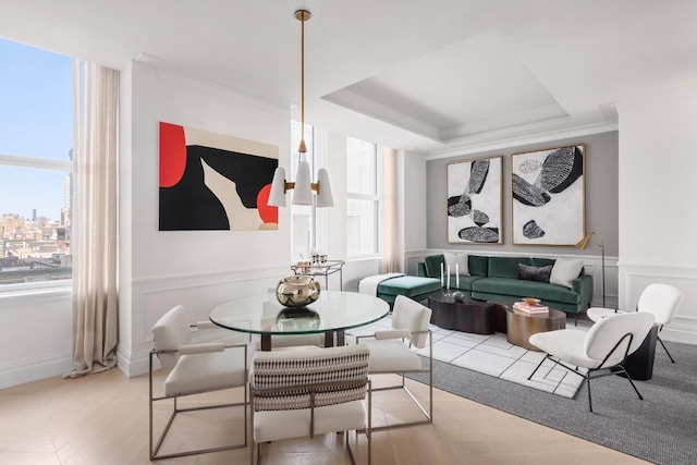 dining space with a tray ceiling, crown molding, and light wood-type flooring