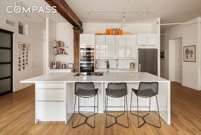 kitchen featuring light hardwood / wood-style flooring, white cabinetry, built in refrigerator, a breakfast bar area, and a kitchen island with sink