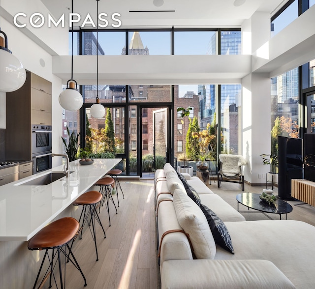 living area with a city view, light wood-style flooring, a wall of windows, and a high ceiling