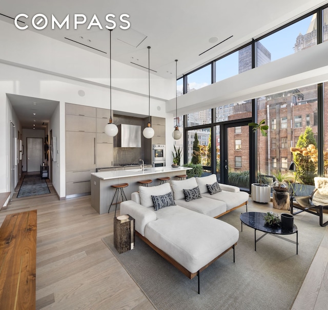 living area with a high ceiling, a wall of windows, and light wood-style floors