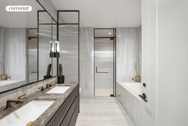 full bath featuring double vanity, a sink, and a relaxing tiled tub