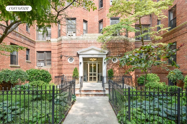 view of exterior entry with cooling unit, fence, and brick siding