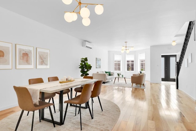 dining room featuring a notable chandelier, light hardwood / wood-style floors, french doors, and a wall mounted air conditioner