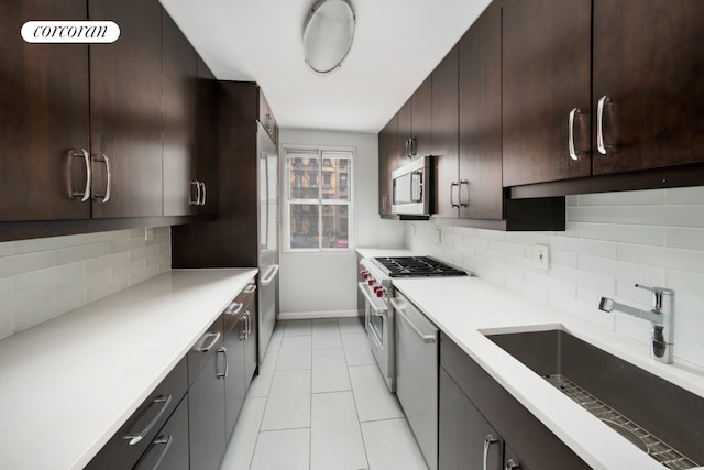 kitchen featuring dark brown cabinetry, decorative backsplash, appliances with stainless steel finishes, light countertops, and a sink