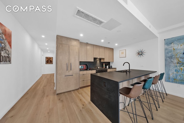 kitchen featuring dark countertops, visible vents, light brown cabinetry, a breakfast bar area, and a sink