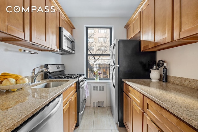 kitchen featuring light tile patterned floors, appliances with stainless steel finishes, brown cabinets, light stone counters, and a sink