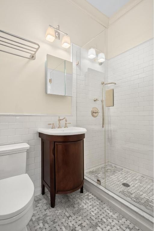 full bathroom featuring tile walls, toilet, wainscoting, a shower stall, and vanity