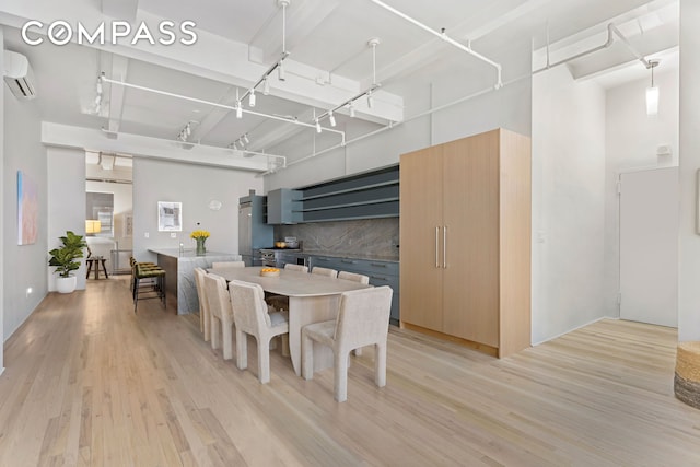 dining space with light wood finished floors, a high ceiling, rail lighting, and a wall mounted air conditioner