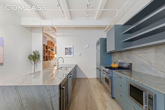 kitchen featuring tasteful backsplash, appliances with stainless steel finishes, light wood-style floors, a sink, and light stone countertops