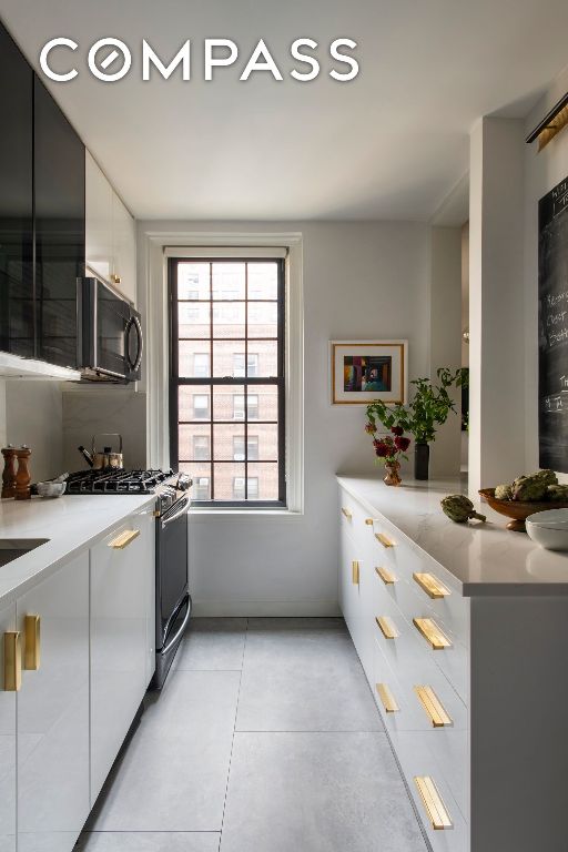 kitchen featuring light tile patterned floors, white cabinets, light countertops, black microwave, and gas stove