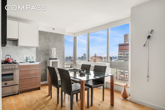 dining area featuring light wood-type flooring, a view of city, and baseboards