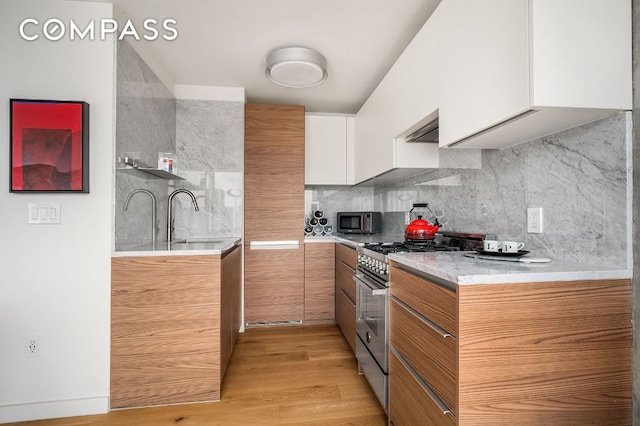 kitchen with stainless steel gas stove, brown cabinetry, white cabinets, light countertops, and a sink