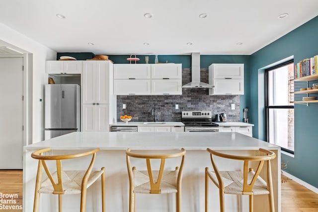 kitchen with appliances with stainless steel finishes, wall chimney range hood, light countertops, white cabinetry, and a kitchen island