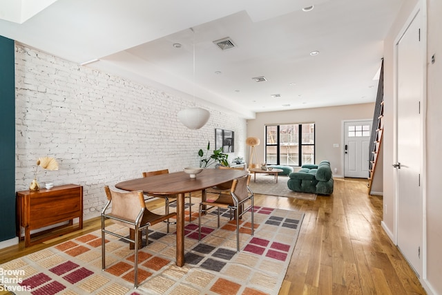 dining space featuring brick wall, light wood finished floors, visible vents, and baseboards