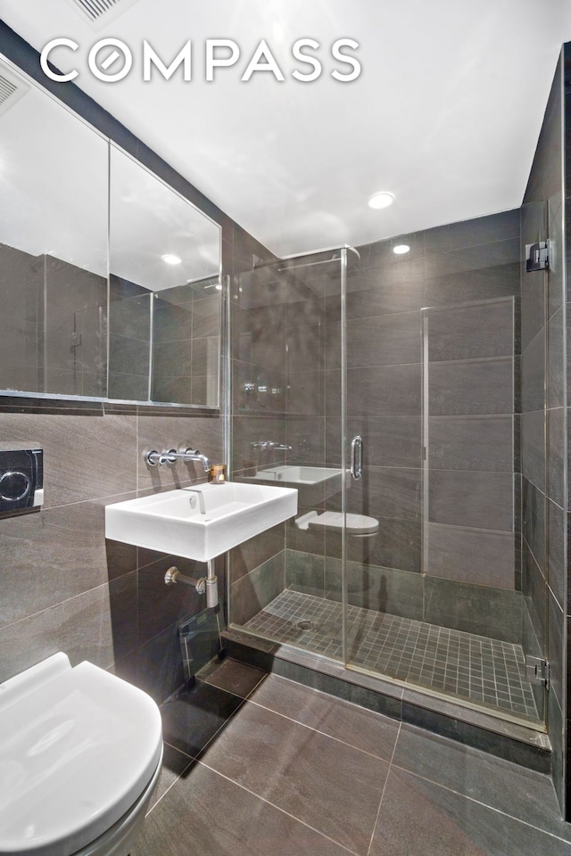 full bathroom with tile walls, a stall shower, a sink, tile patterned floors, and toilet