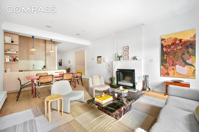 living room with light wood-style floors, a brick fireplace, and crown molding