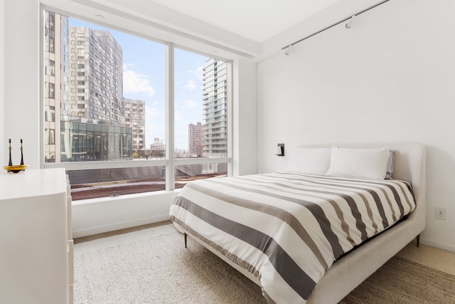 bedroom with a view of city, carpet flooring, rail lighting, and baseboards