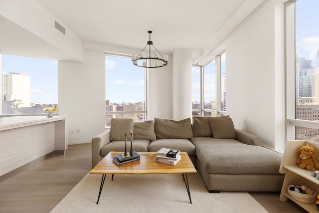 living room featuring an inviting chandelier, light wood finished floors, a view of city, baseboards, and visible vents