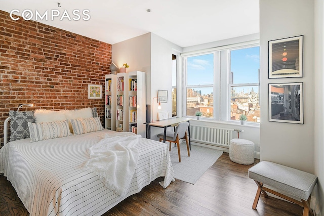 bedroom featuring brick wall, radiator heating unit, and wood finished floors