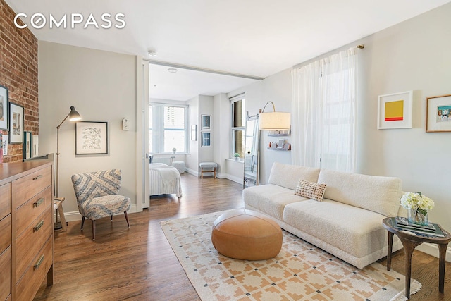 living room featuring brick wall, baseboards, and wood finished floors