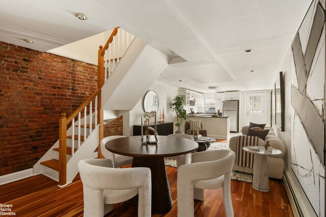 dining space featuring stairs, brick wall, a baseboard radiator, and wood finished floors