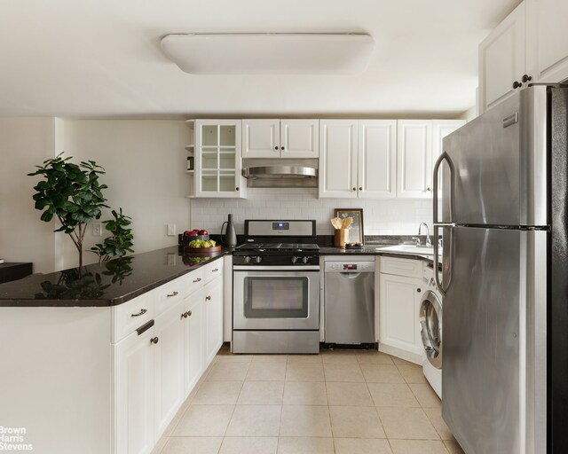 kitchen featuring under cabinet range hood, stainless steel appliances, a peninsula, tasteful backsplash, and washer / dryer