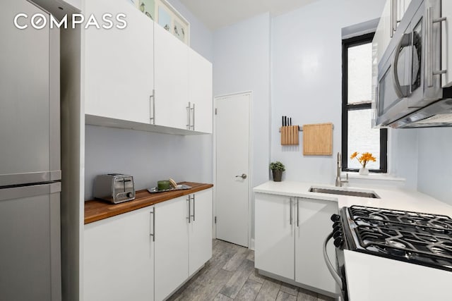 kitchen featuring white cabinetry, freestanding refrigerator, stainless steel microwave, and gas stove