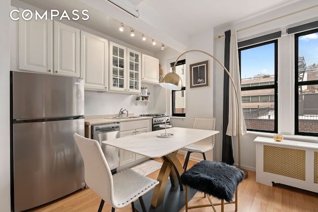 kitchen featuring light wood-type flooring, radiator, appliances with stainless steel finishes, white cabinets, and glass insert cabinets