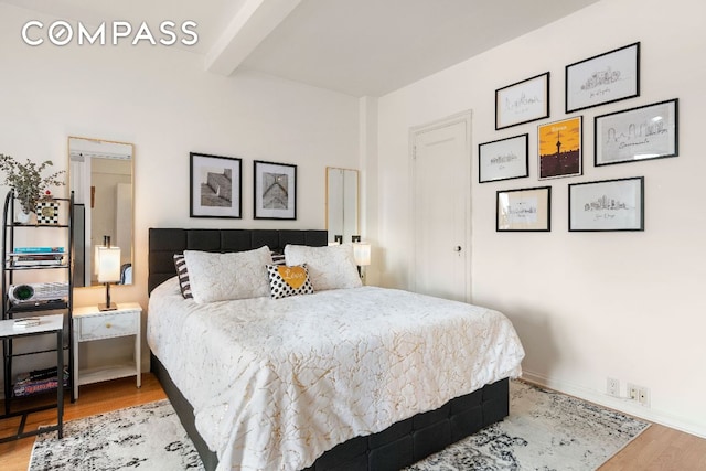 bedroom with beamed ceiling, wood finished floors, and baseboards