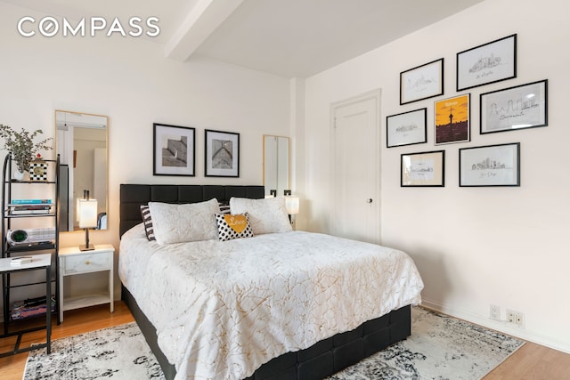 bedroom with beam ceiling, wood finished floors, and baseboards