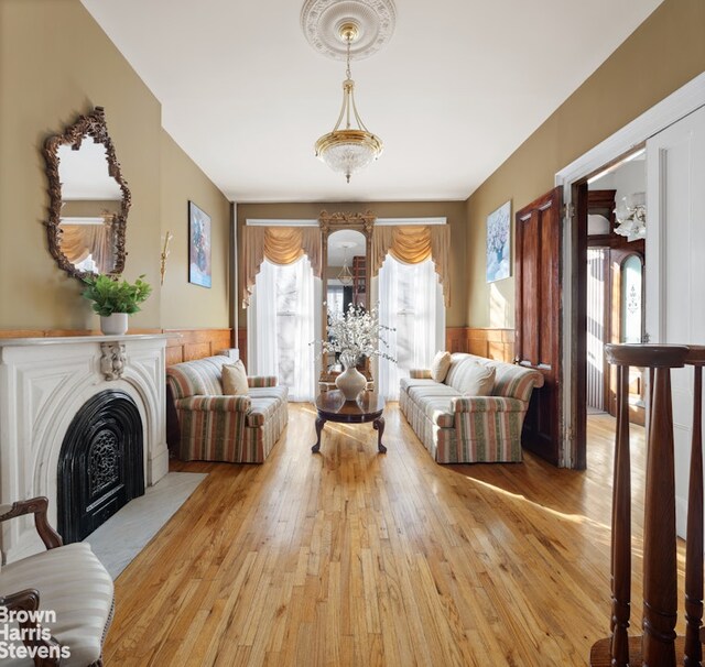 living area featuring a wainscoted wall, light wood-type flooring, and a fireplace with flush hearth