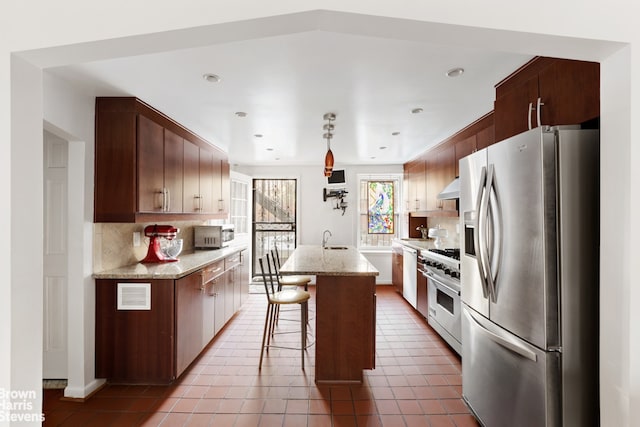 kitchen with a breakfast bar, a sink, a kitchen island, appliances with stainless steel finishes, and wall chimney exhaust hood