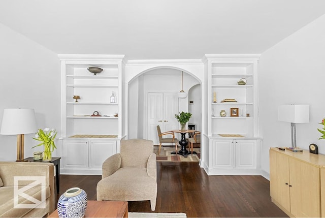 sitting room featuring built in features, arched walkways, and dark wood-type flooring