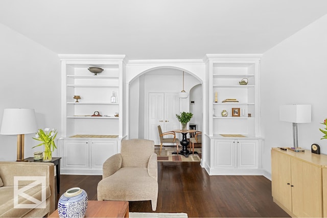 living area with dark wood-style floors, arched walkways, and built in shelves
