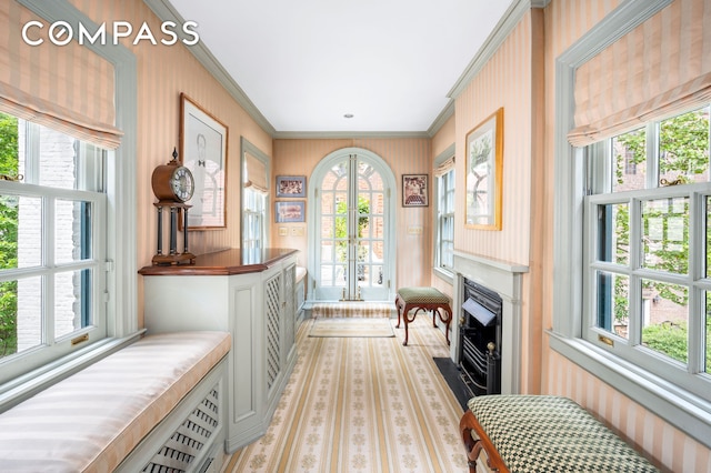 sitting room featuring wallpapered walls, a fireplace with flush hearth, ornamental molding, a wealth of natural light, and french doors