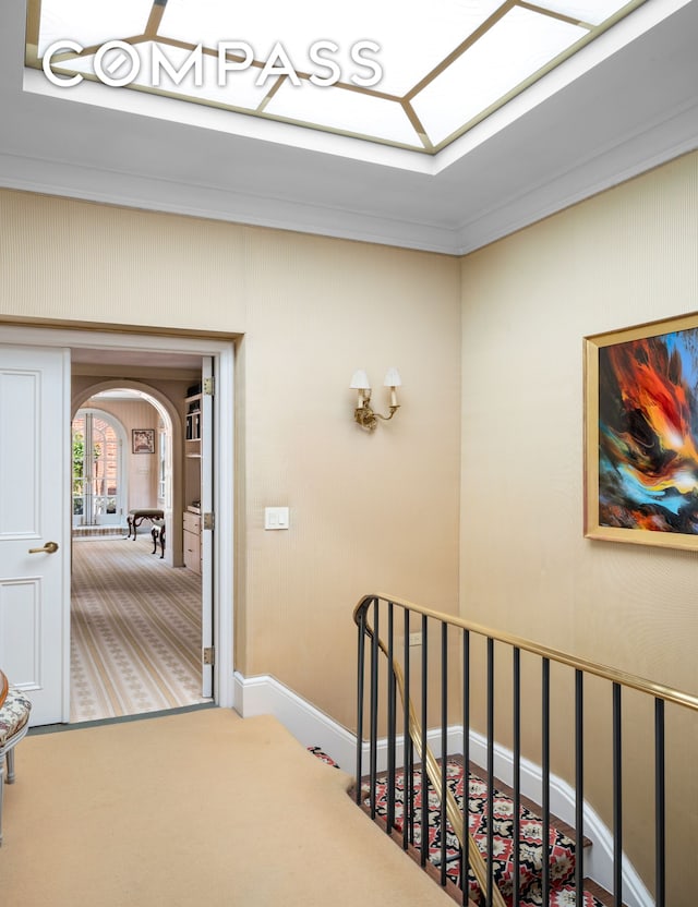 hallway with carpet flooring, crown molding, arched walkways, an upstairs landing, and a skylight