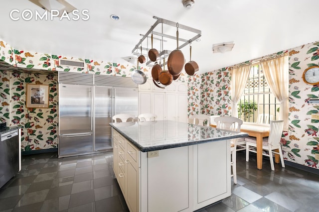 kitchen with white cabinets, appliances with stainless steel finishes, a center island, dark stone countertops, and wallpapered walls