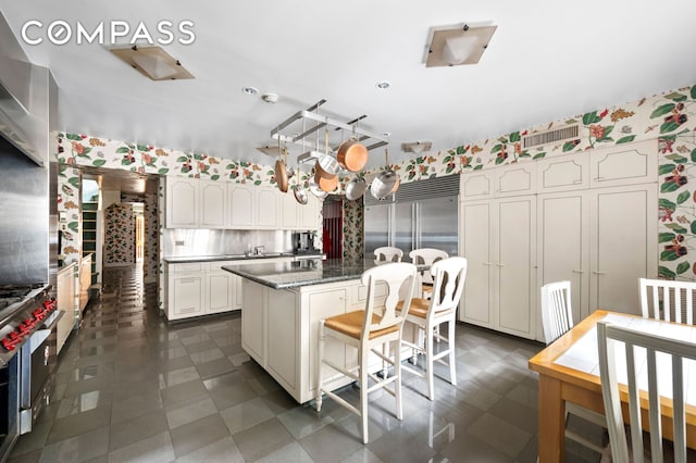 kitchen with a kitchen breakfast bar, a kitchen island, white cabinets, dark floors, and wallpapered walls