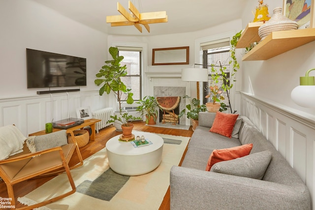 living area with radiator heating unit, plenty of natural light, a high end fireplace, and light wood-style flooring