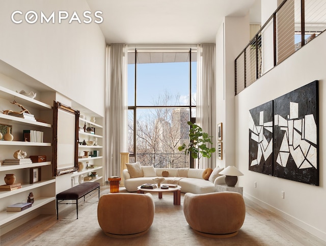 living area with a towering ceiling, baseboards, a wall of windows, and wood finished floors