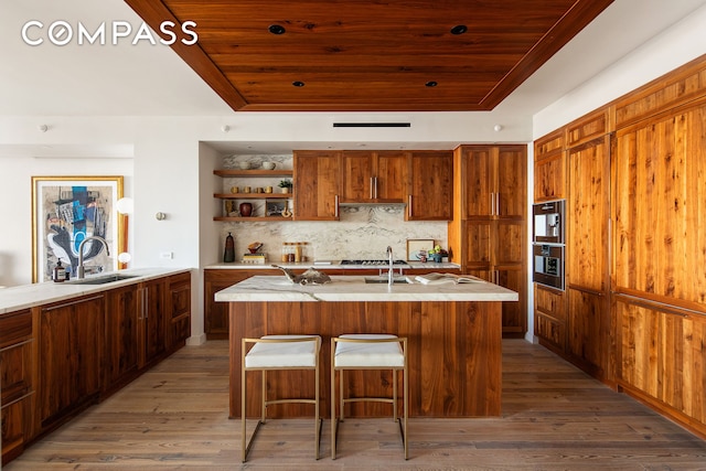 kitchen featuring a tray ceiling, wood ceiling, stainless steel oven, a sink, and wood finished floors