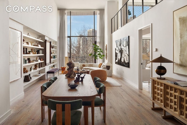 dining room with baseboards, floor to ceiling windows, a towering ceiling, and light wood-style floors