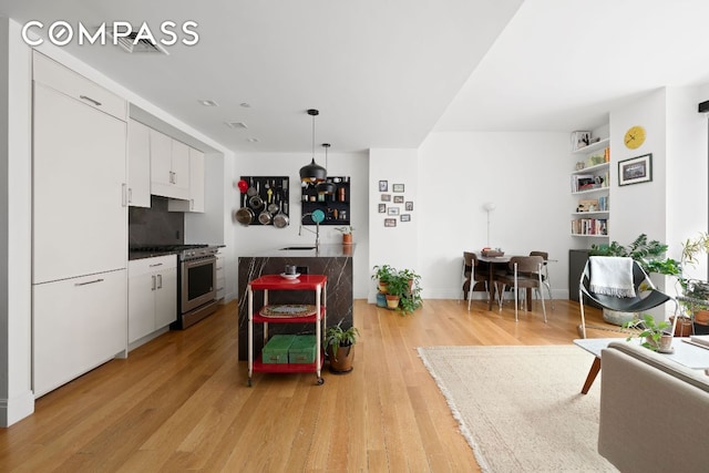 interior space featuring decorative light fixtures, dark countertops, white cabinetry, light wood-type flooring, and high end range