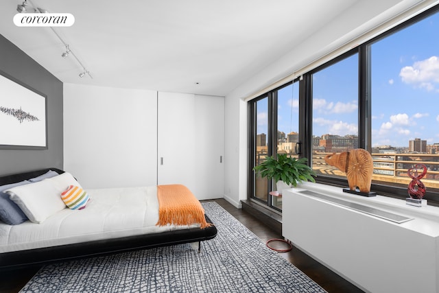 bedroom with visible vents, rail lighting, wood finished floors, and a city view