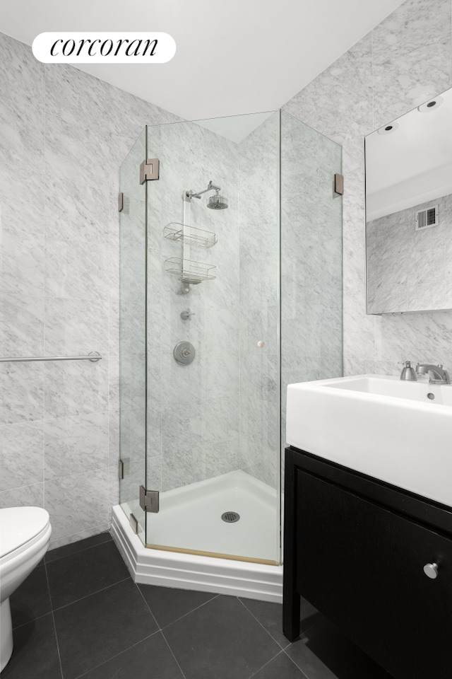 bathroom featuring tile patterned flooring, tile walls, toilet, vanity, and a stall shower