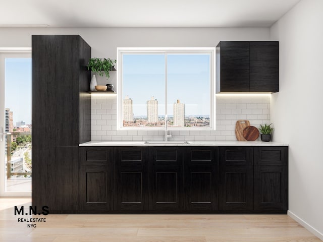 interior space featuring a view of city, light wood finished floors, backsplash, a sink, and baseboards